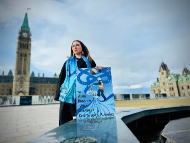 Métis artist Mia Cook from Calgary, Alberta, stands in front of Parliament, proudly showcasing her painting in honor of National Indigenous Water Operator Day. Credit: CIER & Water Movement